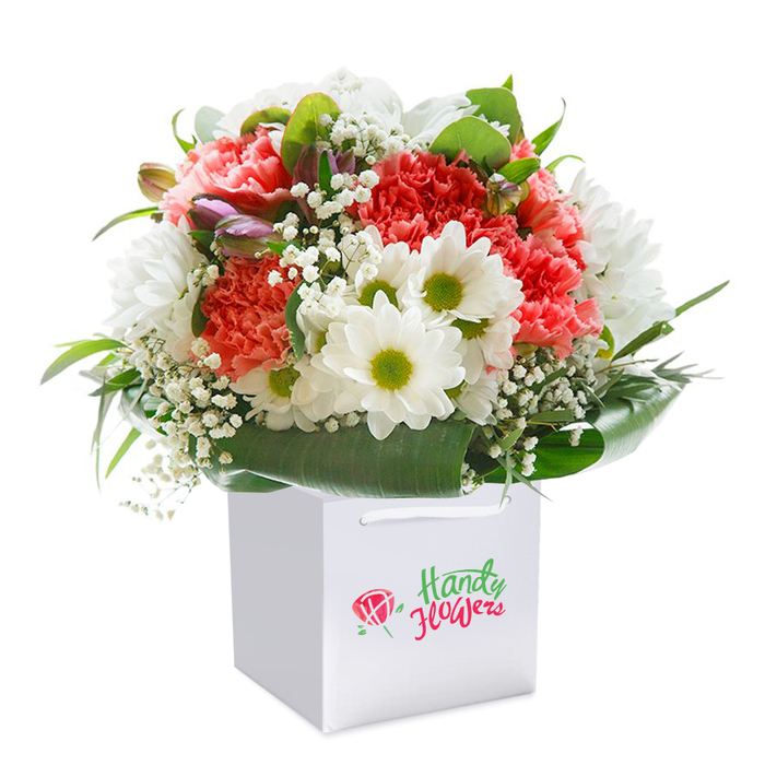 A testament to the artistry of St James's florists, this bouquet combines vivid colour with sophisticated presentation, rising gracefully from a sleek, white square gift bag against a pristine white background. The bouquet unfurls in a cascade of peach and coral carnations whose soft, frilled petals suggest modern opulence, intertwined with proud, white daisy heads lit by vibrant green-yellow centers. Sprigs of baby's breath wind their way throughout, imparting a touch of airiness and subtle, cloud-soft texture. The green framework of glossy, broad-leaf foliage embraces the arrangement and gives it an abundant, formal air-echoing the manicured lawns and tree-lined avenues of St James's. Scattered within are several gently closed buds, kisses of purple at their tips, providing depth and alluding to future blooms. The white gift bag's sturdy ribbon handles elevate the bouquet's portability, ideal for journeys from St James's Park to Covent Garden. Every element, from petal vibrancy to the arrangement's full-bodied profile, is captured under flawless lighting, emphasizing freshness, craftsmanship, and readiness for gifting. Whether destined for a special birthday, anniversary, or a heartfelt gesture, this image captures the boutique experience and impeccable delivery that define St James's floral services.