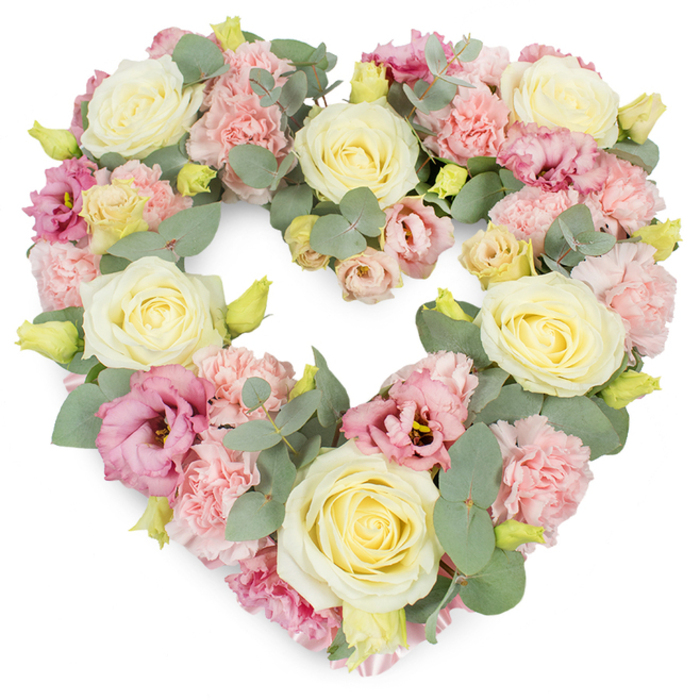 This image shows a meticulously arranged, heart-shaped wreath of funeral flowers, displayed against a bright white background that allows every pastel hue and leaf to stand out clearly. The heart is complete and evenly balanced, its outline formed entirely by layers of lush, fresh blooms. Cream and pale yellow roses serve as the main focal points; their velvety petals are tightly coiled at the centre, then gradually open outward, giving each flower a classic, timeless elegance. Between these roses, clusters of soft pink carnations fill the spaces, their many, finely fringed petals overlapping to create a textured, almost cushion-like effect that lends comfort and warmth. Interwoven throughout are deeper pink and mauve lisianthus blossoms, their more open, slightly rippled petals and darker centres introducing complexity and a gentle richness of colour. Sprays of silvery-green eucalyptus foliage curve gracefully along the heart's edge and through its centre, their rounded leaves offering cool contrast in both tone and shape, and giving harmony to the design. Tiny yellow-green buds appear here and there, suggesting that some flowers are still to unfold, a quiet reminder of life's ongoing rhythm. Every part of the heart is densely filled, so the wreath appears full and luxurious rather than airy, ideal for expressing deep sympathy and enduring love. In the refined setting of St James's, near the elegant streets that border St James's Palace and the theatres of the West End, such a piece would make a thoughtful tribute for a funeral or memorial, capturing both the solemnity of farewell and the tenderness of cherished memories held close to the heart.